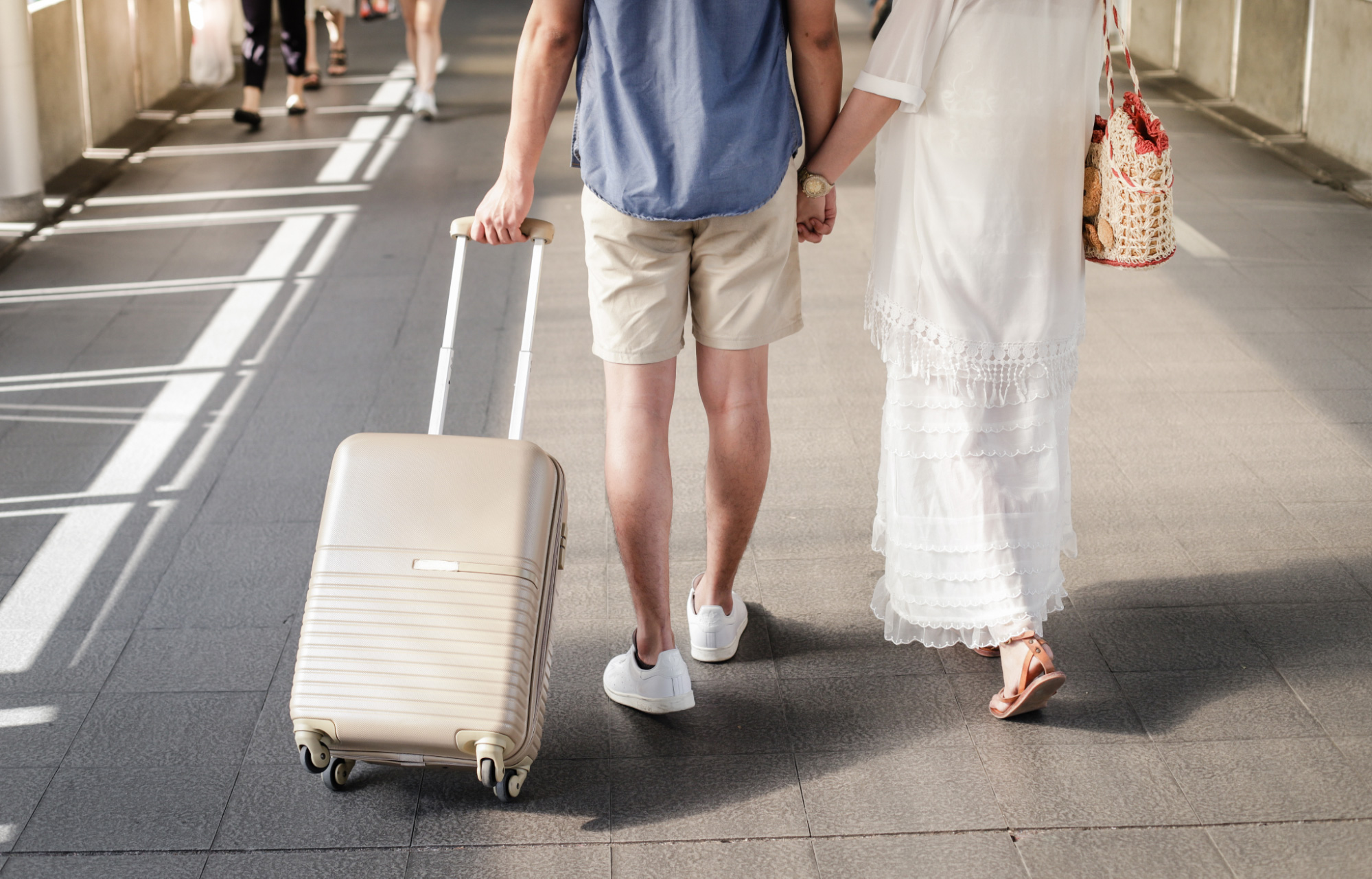 a man is pulling a brown suitcase accompanied by his partner next to him bringing an orange bag at the airport about to head to the best honeymoon destinations in Bali