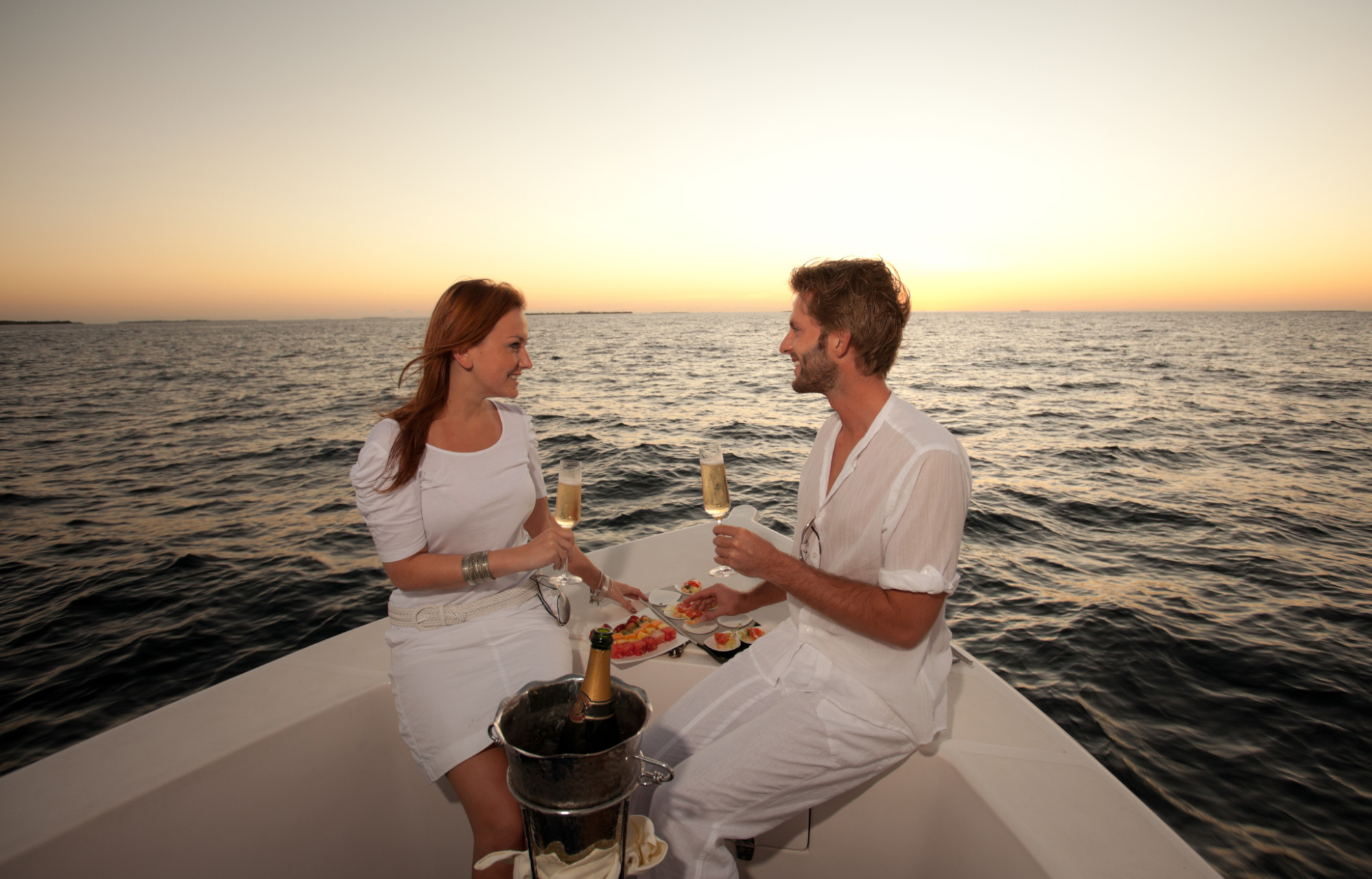 couple sitting on the deck of a luxury yacht enjoying a glass of champagne wearing all white and staying at the best private villas in Bali