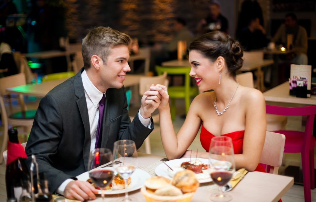 a man wearing a black suit holding the hand of his partner a woman wearing a red dress enjoying romantic fine dining as one of the best things to do in Seminyak