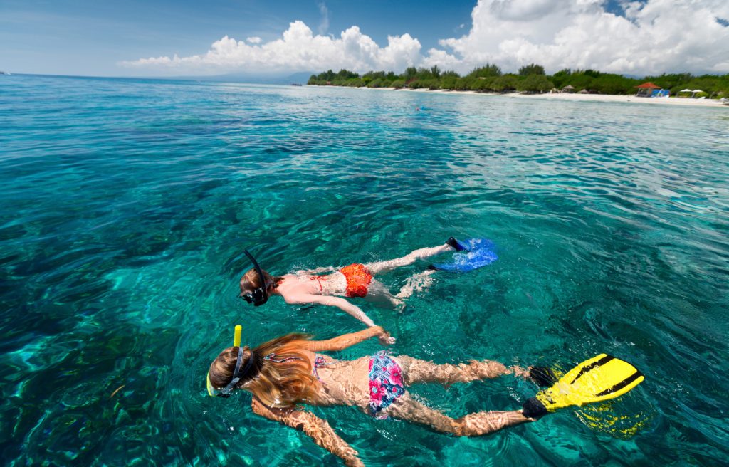 two women wearing red and pink bikinis with floral prints are snorkeling in bali