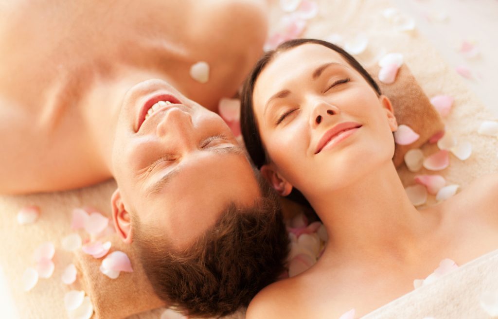 newlyweds lying side by side while closing their eyes with a sprinkling of pink flower petals enjoying a spa in Bali Seminyak