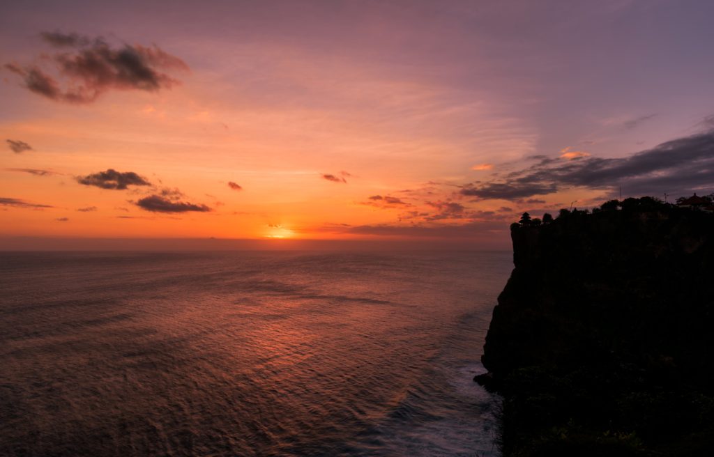 A sunset view with blue, orange, and purple skies coming together from the Uluwatu temple is the best place to visit in Bali for couples