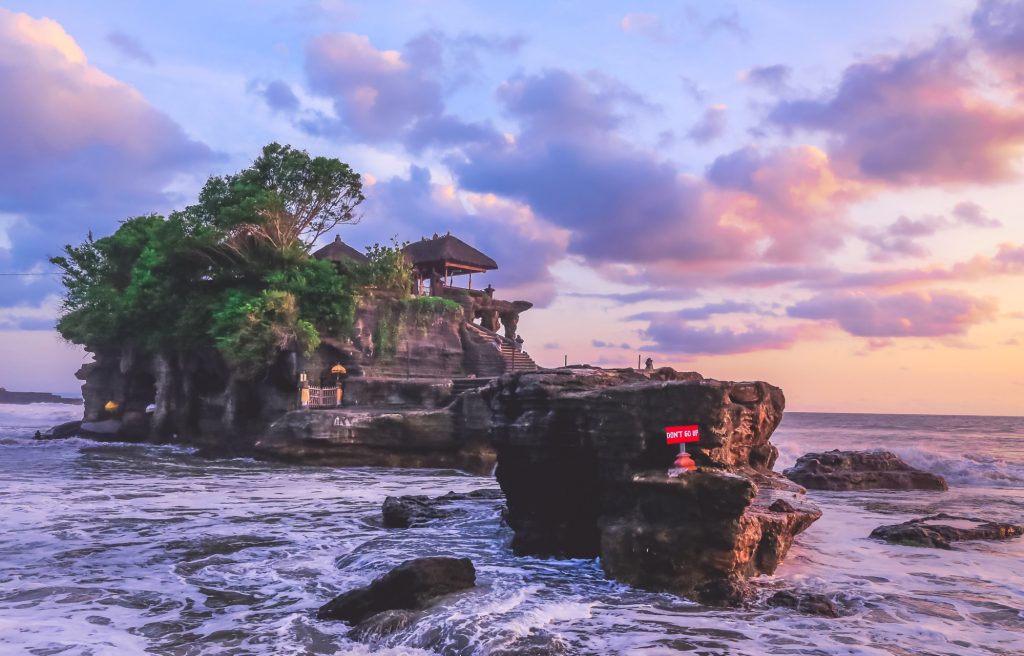 one of the best things to do in Seminyak for couples is to visit Tanah Lot Temple with a stunning sunset view of blue, purple, and orange sky gradations