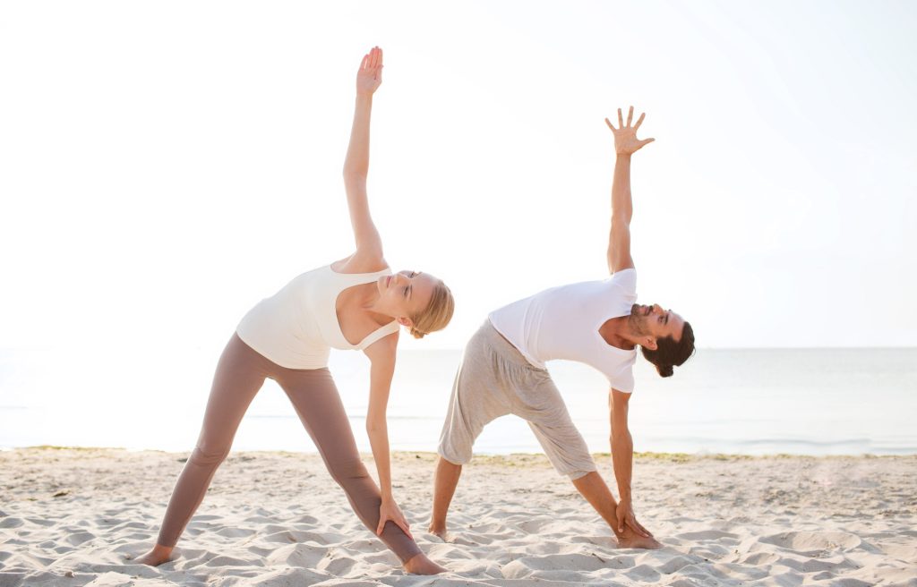 a couple doing a yoga retreat Seminyak poses on the beach wearing white clothes